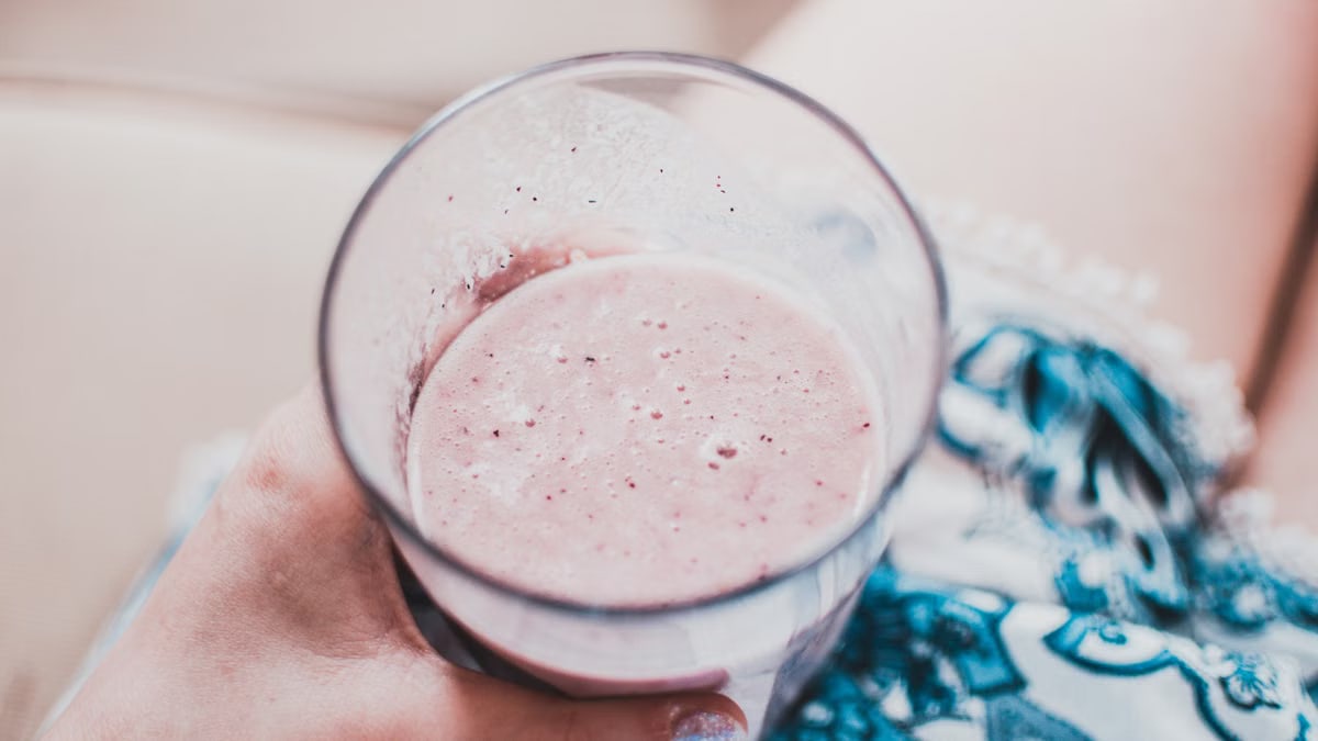 Close-up of a person holding a creamy strawberry smoothie in a glass, perfect for a refreshing treat.